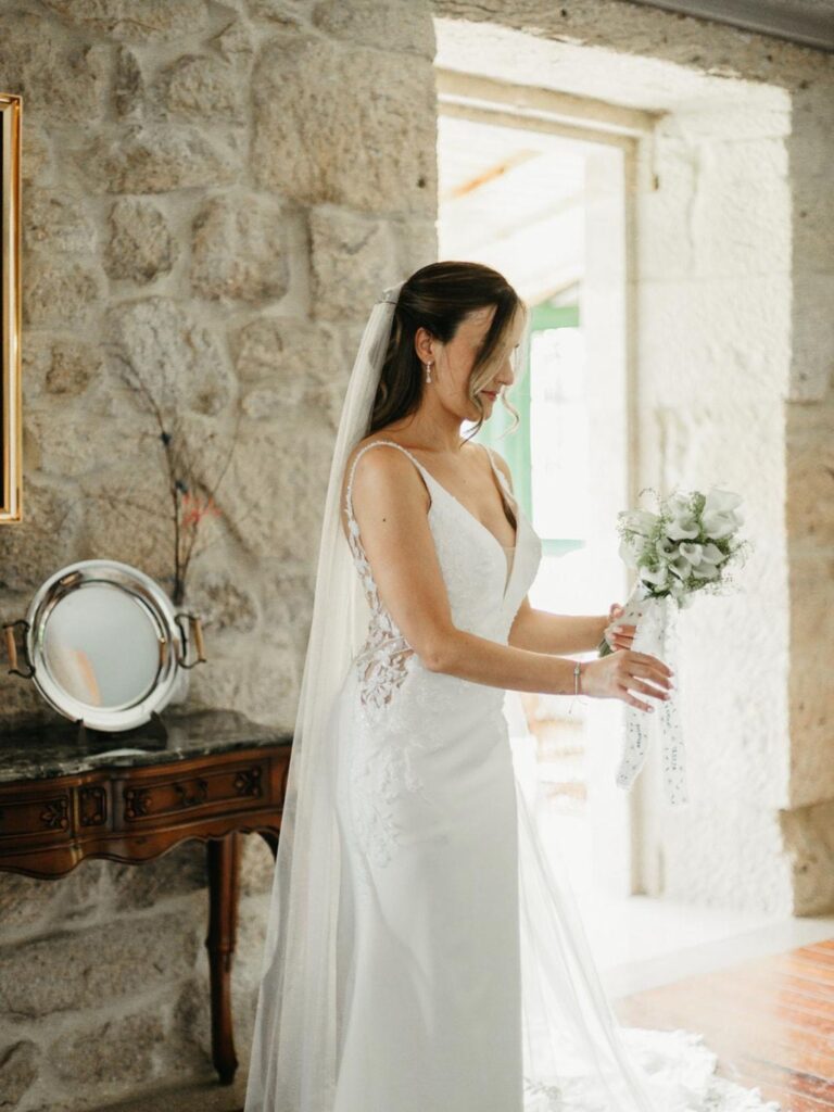 Novia con vestido blanco sujetando el ramo con la cinta bordada personalizada