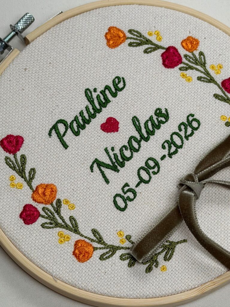 Porta-alianzas bordado en bastidor con los nombres Pauline y Nicolas, la fecha y flores naranjas