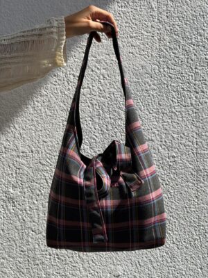 Bolso Camila mini de tartán gris y rosa con cierre de lazo, sujeto en la mano