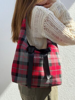 Bolso Camila mini de tartán rojo con lazo negro, llevado al hombro